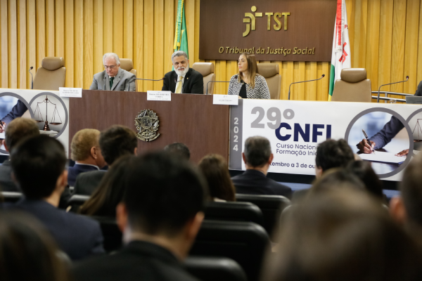 Foto do auditório com os ministros e a presidente da Anamatra na mesa de abertura ao fundo e as cabeças dos participantes em primeiro plano em desfoque.