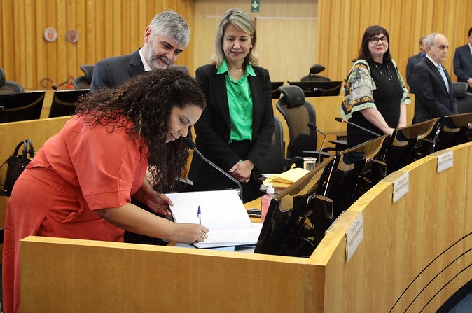 Foto da juíza assinando o termo de posse na plenário de sessão.