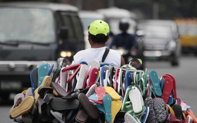 Foto de vendedor ambulante de costas carregando várias sandálias em uma moto.