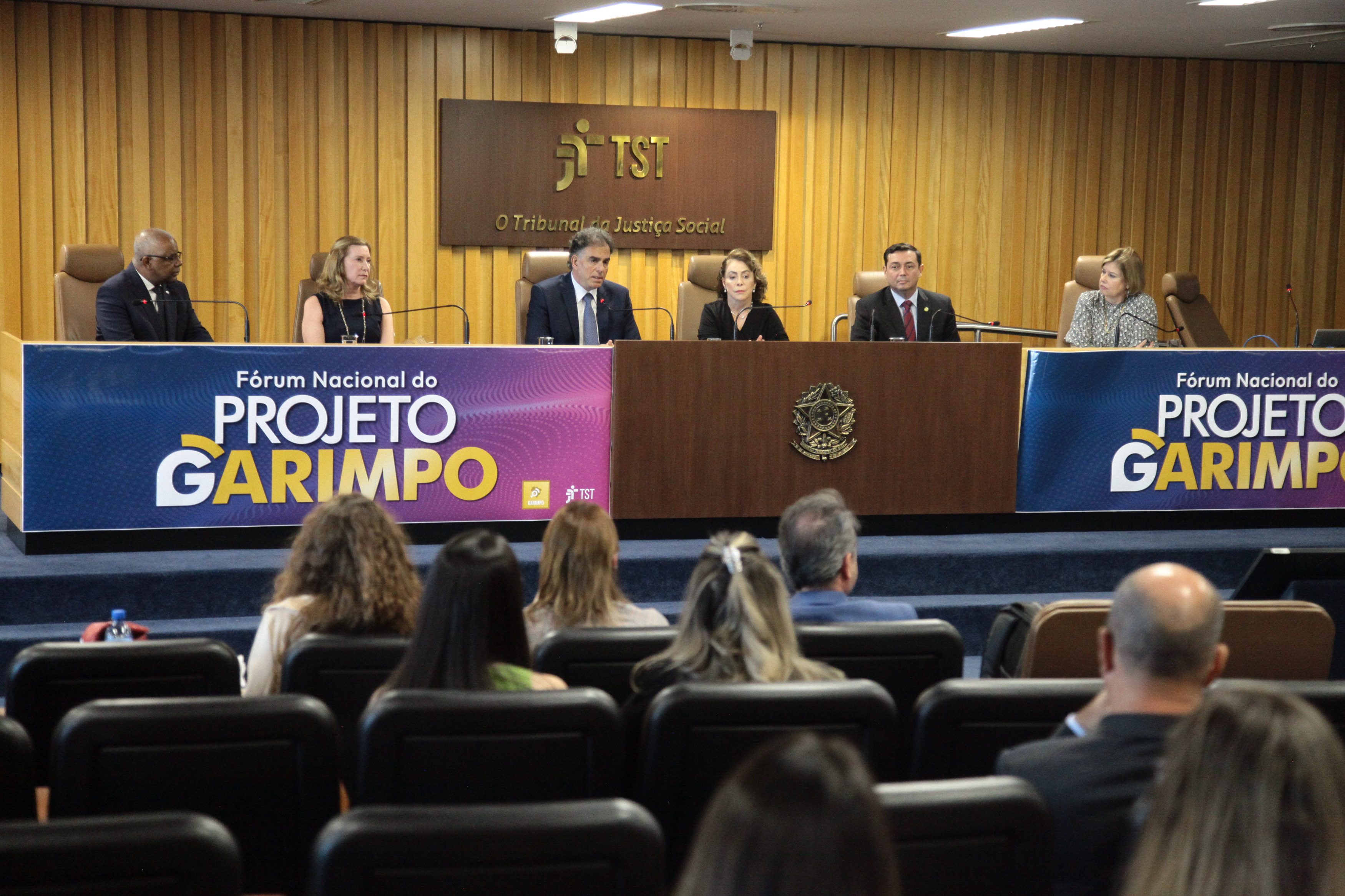 Foto do evento Fórum Nacional do Projeto Garimpo um auditório. Em destaque a mesa do evento com seis pessoas sentadas. 