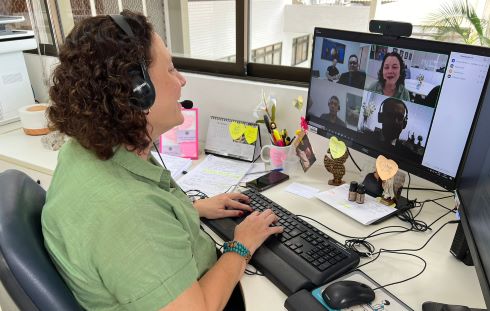 Fotografia de uma reunião online, com a presença de uma mulher teclando e 4 pessoas na chamada de vídeo