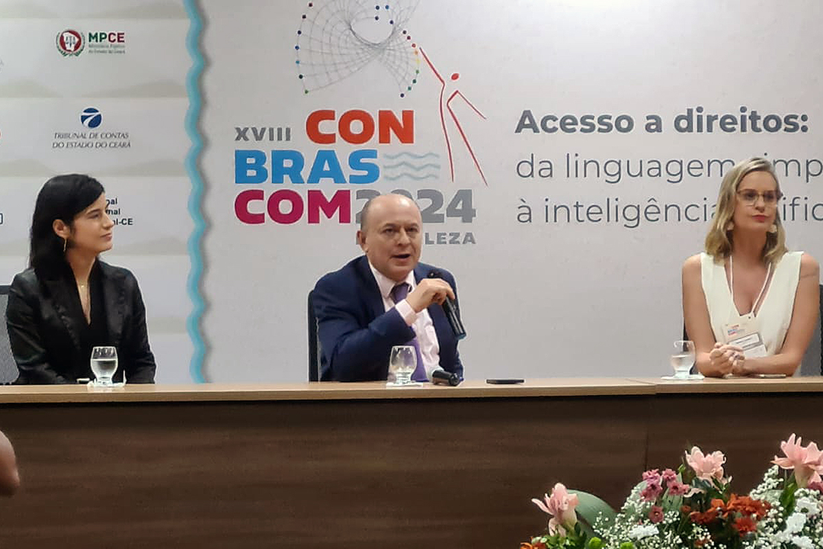 Desembargador Parente aparece no centro com o microfone e, atrás, aparece a XVIII CONBRASCOM 2024 que falou sobre o acesso aos direitos.