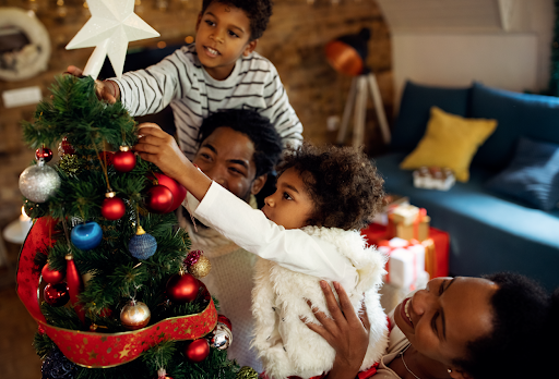 Fotografia com duas crianças e dois adultos decorando uma árvore de Natal