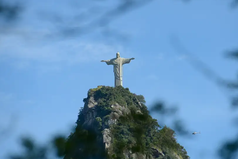 Foto do Cristo Redentor em perspectiva entre galhos de uma arvore abaixo do Corcocavado